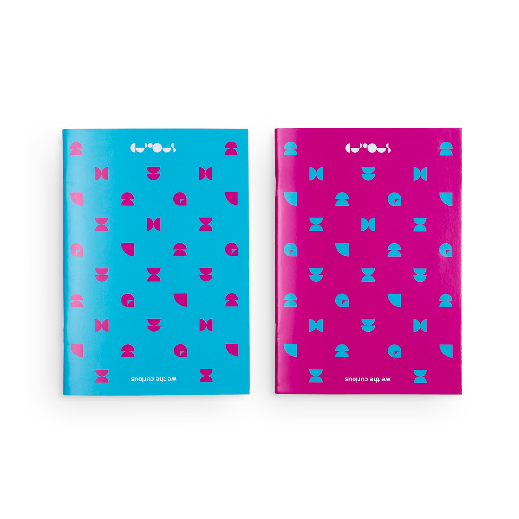 Two notebooks side by side. On the left is a blue notebook with pink pattern. On the right is a pink notebook with blue patterns. At the top of both notebooks is the we the curious logo in white. At the bottom of each notebook is the name 