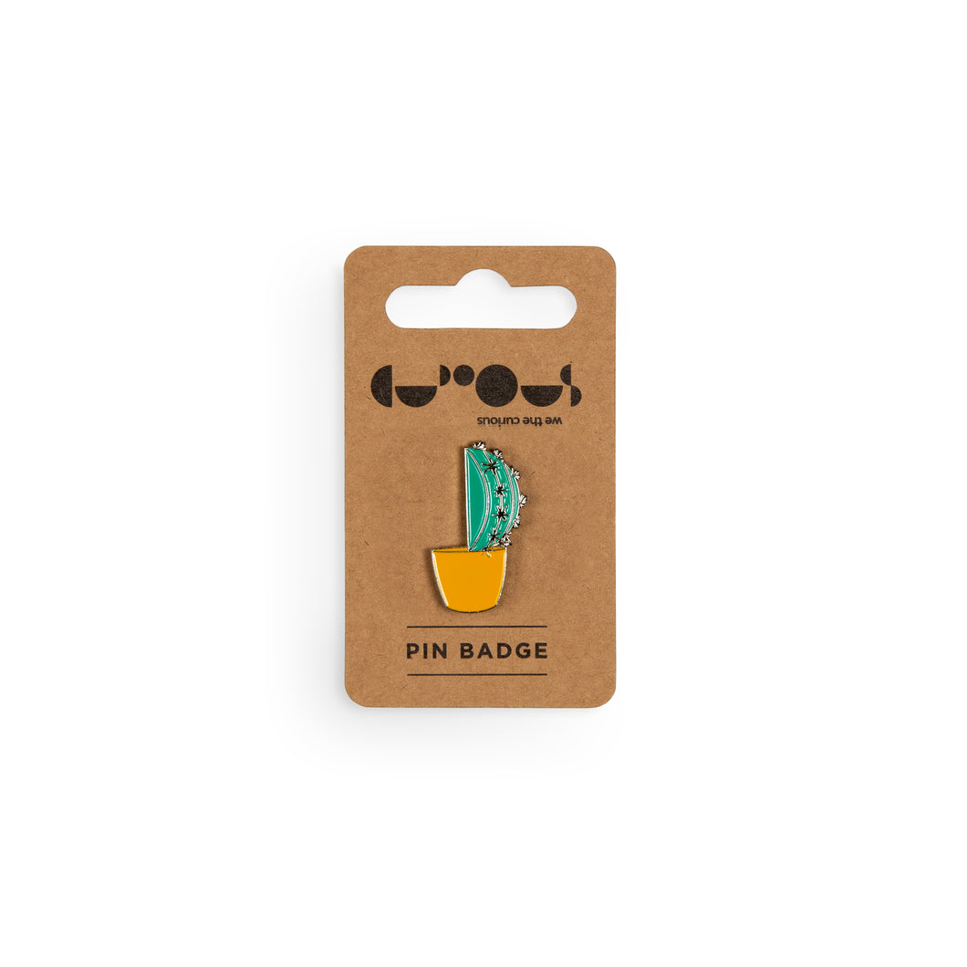 Green cactus in orange pot pin badge sits on a brown cardboard backer with We The Curious logo and the phrase 